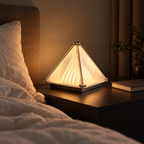 Warm pyramid desk lamp on a bedroom nightstand beside a bed