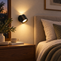 Black rotating double-head rechargeable LED wall sconce beside a bed