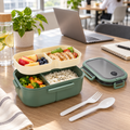 Green double-layer compartment lunch box open with a packed meal in a modern office